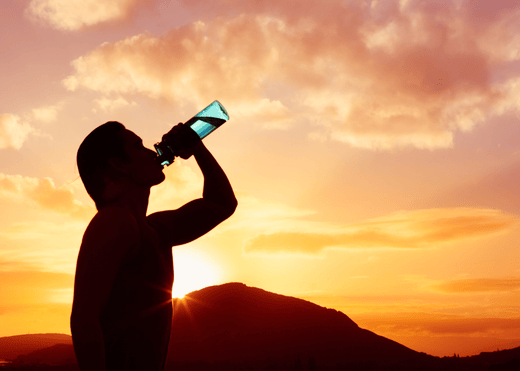 Man drinking water outdoors under bright sun, with healthy hair and skin emphasized.