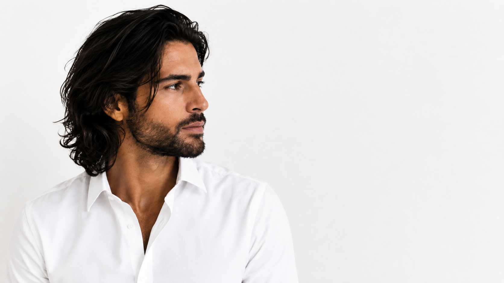 A man with dark hair and a beard wearing a white button-down shirt, shown in profile against a plain white background.